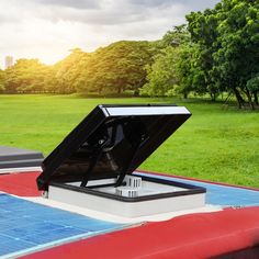 an open roof box on top of a red and white car in a park with trees