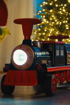 a small toy train with lights on is in front of a christmas tree