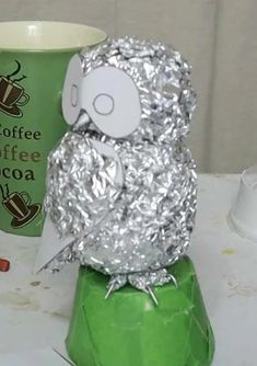 an owl made out of tin foil sitting next to a coffee cup