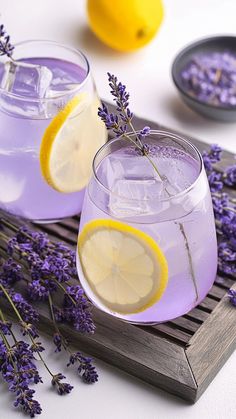 two glasses filled with lavender lemonade on a wooden tray next to sliced lemons