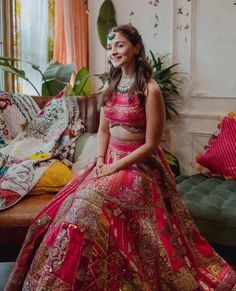 a woman in a red and gold lehenga sitting on a couch