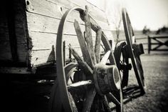 an old wooden wagon wheel leaning against a wall in black and white with the sun shining on it