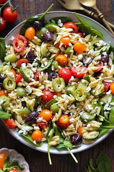 a bowl full of pasta salad with tomatoes, olives and feta cheese