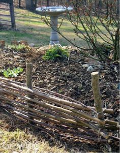 a wooden fence made out of sticks in the grass next to a birdbath