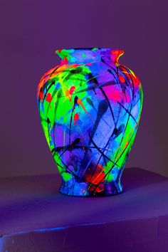 a brightly colored vase sitting on top of a purple tableclothed surface in front of a dark background