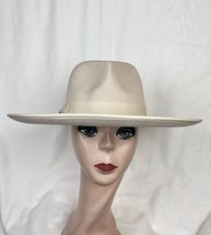 This beige felt flat brim 4-inch fedora with pinched fedora crown has a 1  1/2 inch grosgrain ribbon with a bow around the crown and an elastic tie in the crown which will fit up to 22 7/8 inch head size. The inside band has a sizing cord to adjust to your head size. The brim has a ribbon edging. NOTE: Please check the head size before purchase, I am happy to answer any questions you may have. There will be a 20% restocking fee for all returned hats. Classic Beige Fedora Felt Hat, Fitted Beige Wide Brim Fedora, Beige Brimmed Fur Felt Fedora, Beige Fur Felt Brimmed Fedora, Classic Cream Fedora For Winter, Beige Fitted Felt Hat With Flat Crown, Fitted Beige Fedora Hat, Beige Fitted Fedora Hat, Classic Cream Winter Fedora