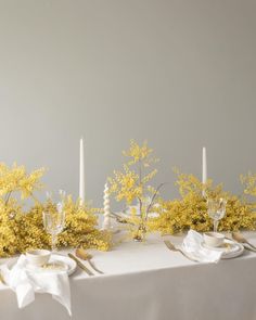 the table is set with yellow flowers, candles and napkins for an elegant dinner