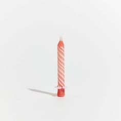 a pink and white striped candle on a white surface with a shadow from the top