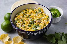 a bowl filled with corn and salsa next to tortilla chips, lime wedges and cilantro