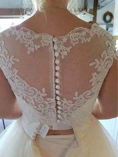 the back of a woman's wedding dress with white lace and buttons on it