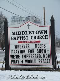 a church sign in front of a snow covered field with power lines and houses behind it