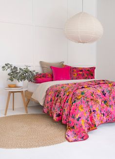 a white bedroom with pink and yellow bedding, pillows and rugs on the floor