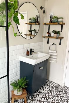 a bathroom with black and white tile flooring next to a sink, mirror and potted plants