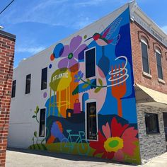 a building painted with colorful flowers and birds on it's side in front of a brick building