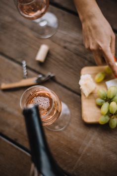 a person cutting up grapes on top of a wooden table next to two wine glasses