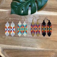 six pairs of beaded earrings sitting on top of a wooden table next to a green leaf