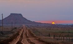 the sun is setting over a dirt road in front of a large mountain with barbed wire