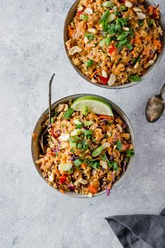 two bowls filled with rice and vegetables on top of a white table next to spoons