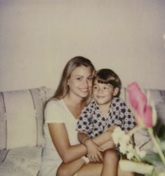 a woman sitting next to a child on top of a couch with a rose in front of her