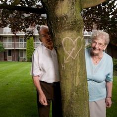 an older couple standing next to a tree with a heart drawn on it