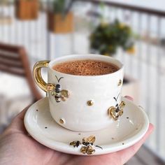 a person holding a cup of coffee with gold decorations on the rim and saucer