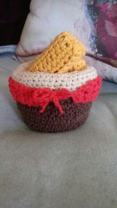 a crocheted cupcake sitting on top of a bed next to a pillow