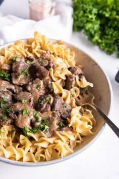 a white bowl filled with pasta and meat covered in gravy next to parsley