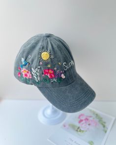 a hat with embroidered flowers on it sitting on top of a white table next to a card