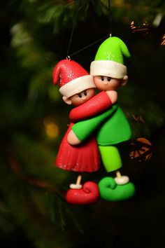 an ornament hanging from a christmas tree with two elves hugging and holding each other