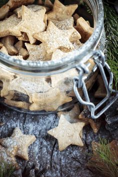 a glass jar filled with star shaped cookies on top of a wooden table next to pine branches