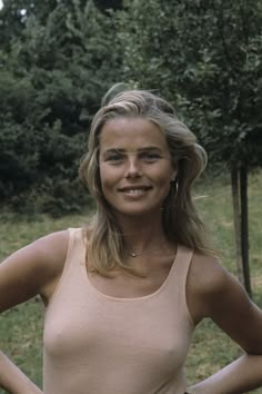 a woman standing with her hands on her hips and looking at the camera while wearing a tan tank top