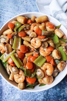 a white bowl filled with shrimp, carrots and corn on top of a blue table