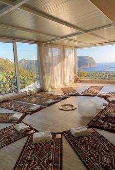 a room with lots of rugs on the floor and large windows looking out onto the ocean