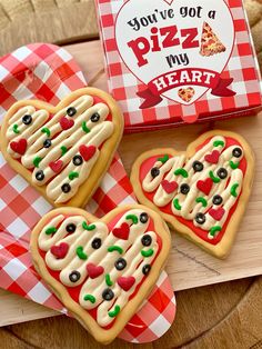 three heart shaped cookies sitting on top of a wooden tray next to a box of pizza