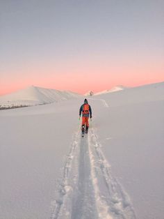 a man riding skis down a snow covered slope at sunset or dawn in the mountains