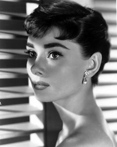 a black and white photo of a woman in front of shutters looking at the camera