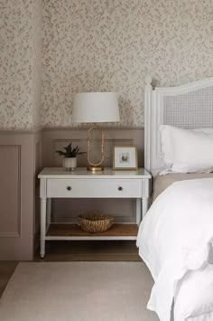 a white bed sitting next to a nightstand with a lamp on top of it in a bedroom