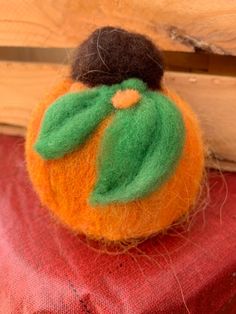 an orange with a green leaf on it sitting on a piece of cloth next to a wooden plank