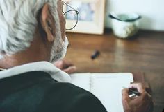 an old man sitting at a desk writing on a notebook - stock photo - images