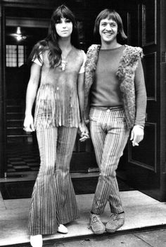 two young women standing next to each other in front of a store door wearing striped pants and vests