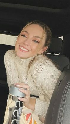 a woman sitting in the back seat of a car holding a drink and smiling at the camera