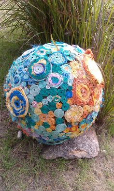 a large ball made out of buttons sitting on top of a rock in the grass