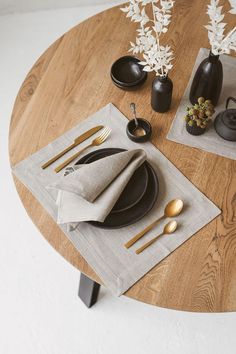 a wooden table topped with black plates and silverware