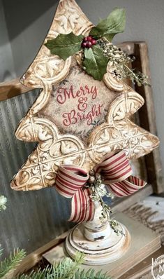 a christmas ornament on top of a table with holly and red ribbon around it