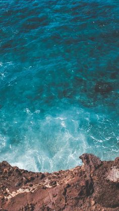 two people on surfboards in the water near some rocks and blue water with white foam