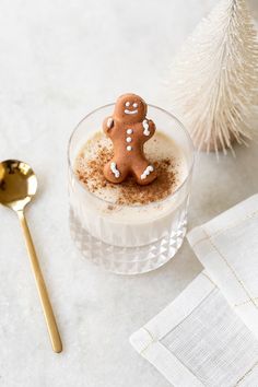 a glass with some food in it next to a gold spoon and a white christmas tree