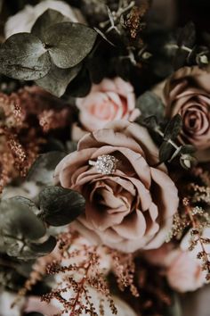 an arrangement of flowers and greenery with a diamond ring