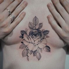 a woman's chest with a rose tattoo on her chest and hands holding it