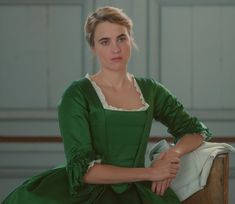 a woman in a green dress sitting on a chair with her hand on her hip