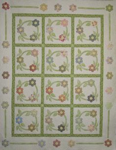 a quilted wall hanging with flowers and leaves on the front, along with a green border